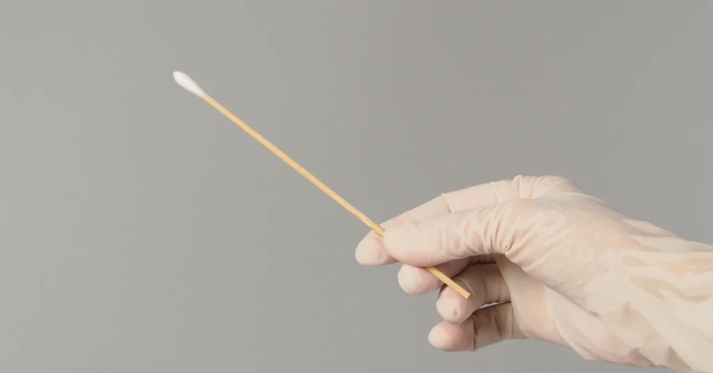 Hand holding a cotton swab to treat mealybugs on a plant with rubbing alcohol