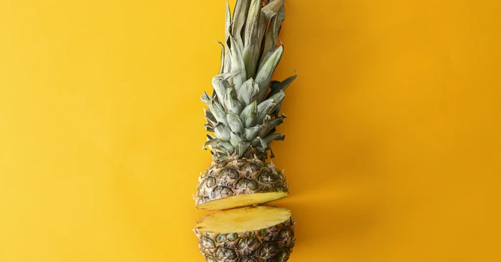 Pineapple on a yellow background being cut to remove the leafy crown