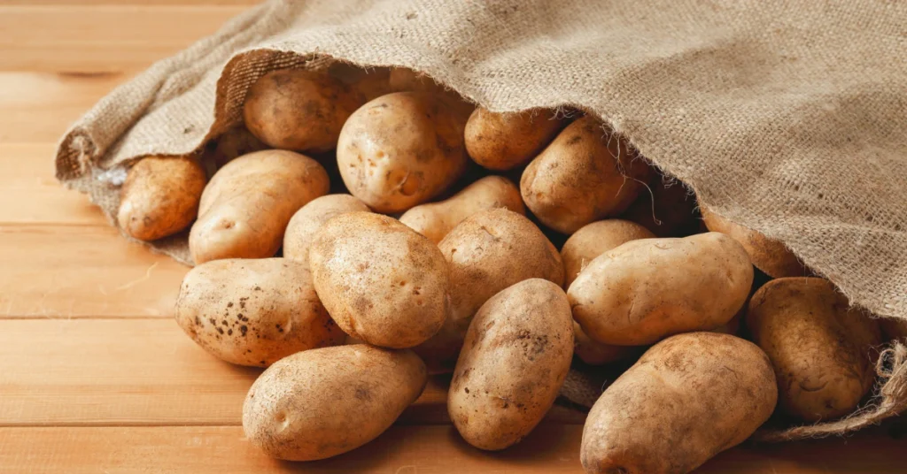 Harvested potatoes spilling out of a burlap sack onto a wooden surface