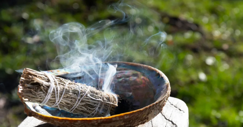 Burning sage smudge stick with smoke rising from a bowl outdoors