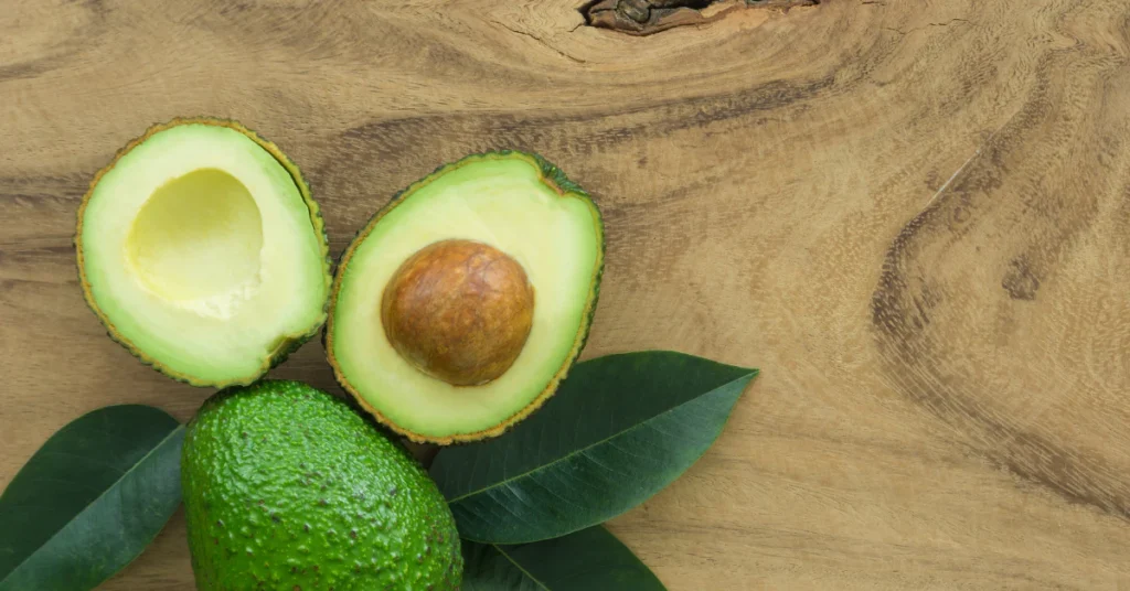 Cut avocado halves and a whole green avocado on a wooden table